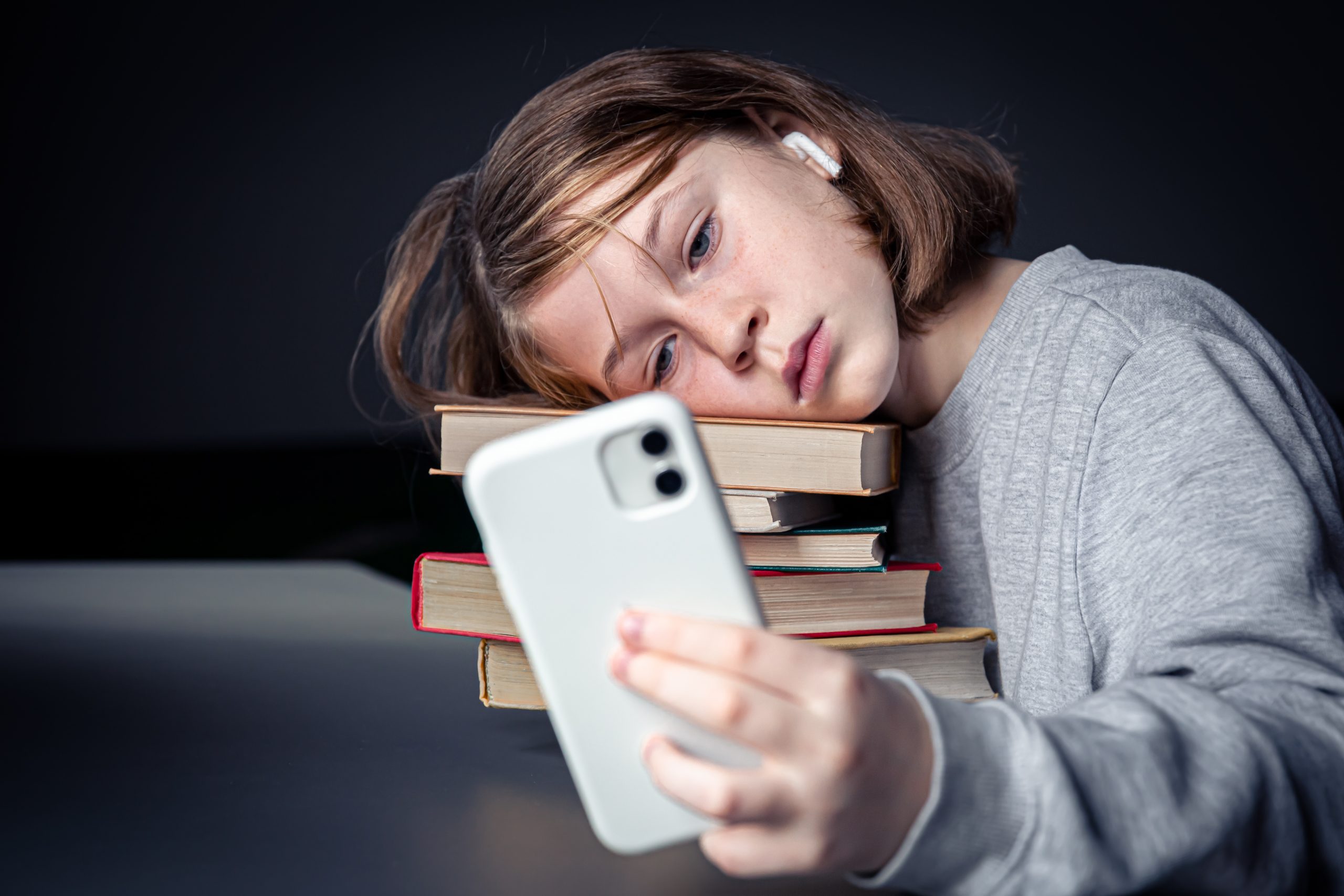 A little girl sits near books and takes a selfie, bored from reading.